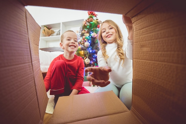 O menino feliz e uma menina abrem a caixa no fundo da árvore de natal