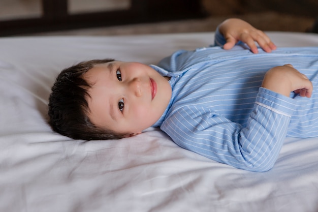 O menino feliz no pijama azul encontra-se na cama da casa, vista de cima, espaço para texto