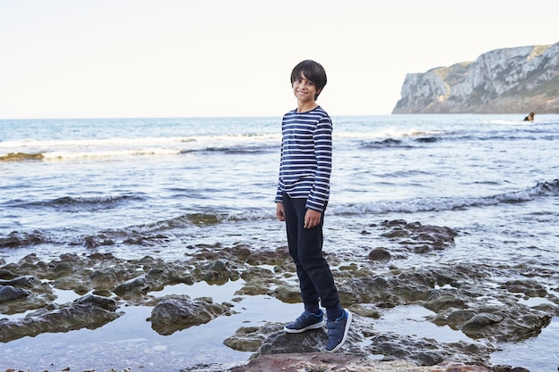 O menino fica em uma rocha à beira-mar