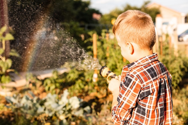 O menino gosta de um arco-íris enquanto rega no jardim