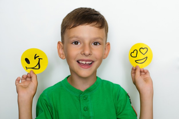 O menino mostra emoções e segura sorrisos engraçados feitos de papel