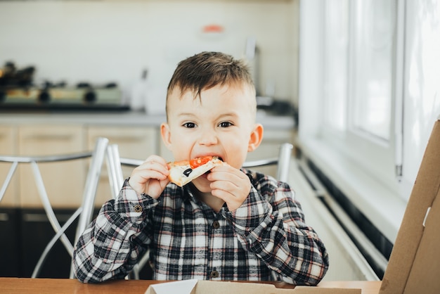 O menino na cozinha em casa comendo pizza com salmão