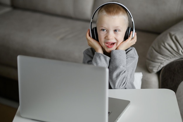 O menino no PC ouve música e canta segurando fones de ouvido com as mãos