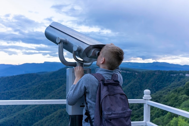 O menino olha pelo telescópio com curiosidade observando a montanha olhando para o céu através