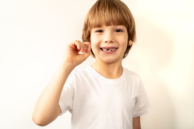 O menino segura um dente de leite caído na mão e sorri