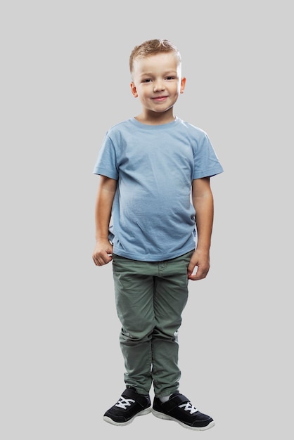 O menino tem 5 anos. Uma criança de jeans e camiseta azul. Isolado em um fundo cinza claro. Altura toda. Vertical.