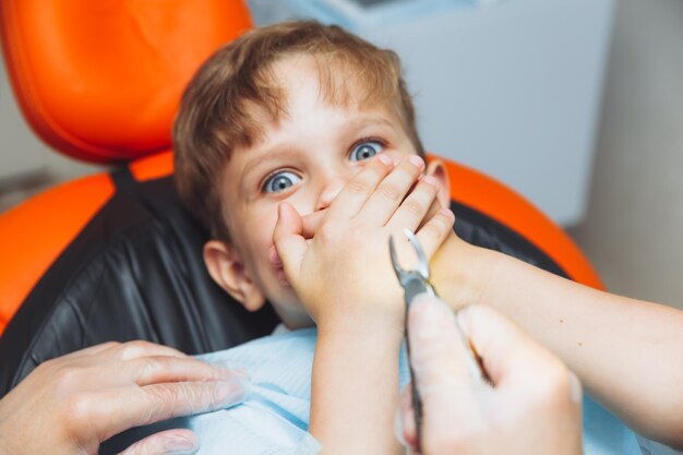 O menino tem medo do dentista com fórceps a criança tem medo de remover o dente o adolescente se recusa a tratar seus dentes conceito de odontopediatria