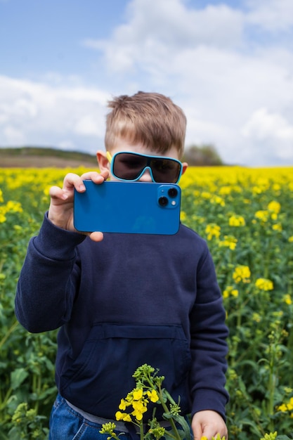 O menino tira fotos da paisagem de verão canola em um smartphone