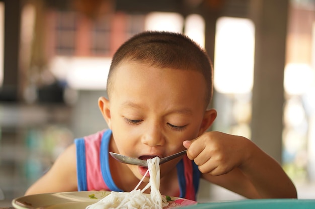 O menino usa uma colher para colocar macarrão na boca para comer