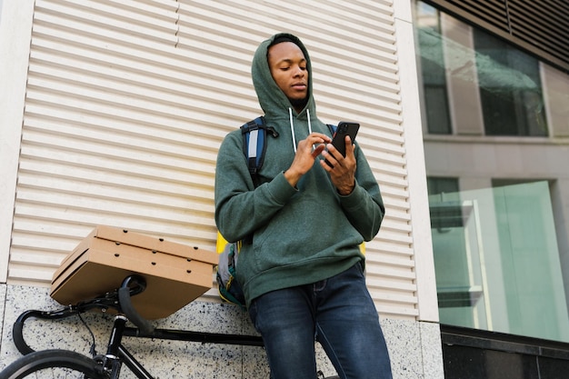 O mensageiro pedalou até o endereço do cliente e está esperando por ele O entregador está digitando no telefone