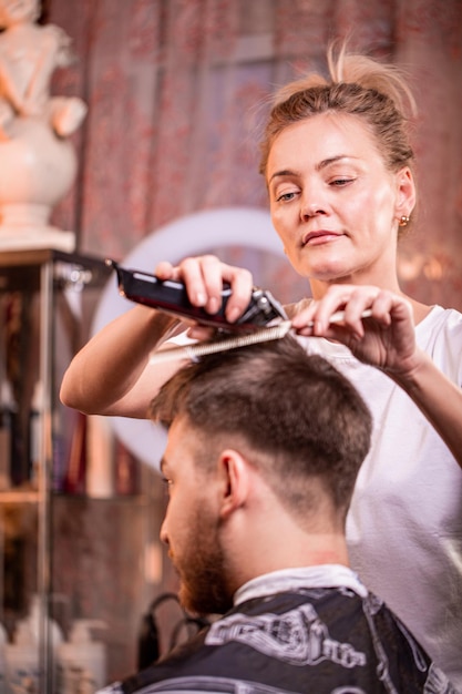 Foto o mestre corta o cabelo e a barba de um homem em uma barbearia um cabeleireiro faz um corte de cabelo para um jovem conceito de beleza autocuidado