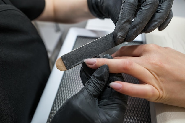 O mestre das serras de manicure e anexa uma forma de unha durante o procedimento de extensões de unhas no salão de beleza Cuidado profissional para as mãos