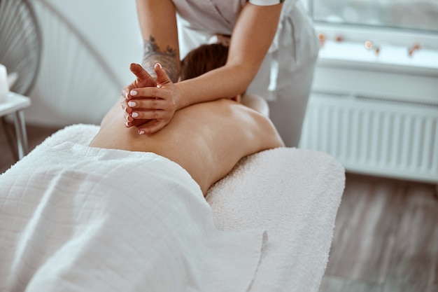 O mestre de massagem profissional confiante está fazendo procedimentos para uma mulher caucasiana em estilo minimalista moderno