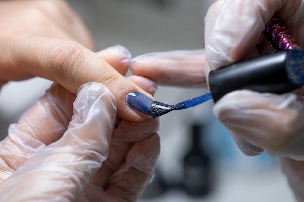 O mestre do serviço de unhas faz unhas de manicure fechadas nas quais é aplicado um esmalte de gel azul
