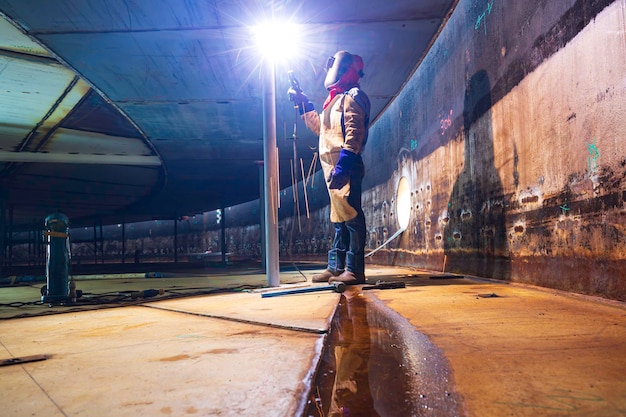 O metal do trabalhador masculino de soldagem faz parte da construção do feixe do tanque do telhado da placa de máquinas faísca dentro de espaços confinados