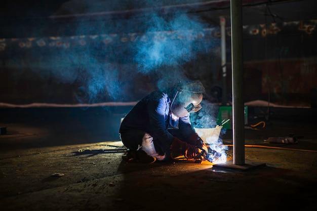 O metal do trabalhador masculino de soldagem faz parte da construção inferior da placa do tanque de máquinas, tanque de armazenamento de petróleo e gás dentro de espaços confinados