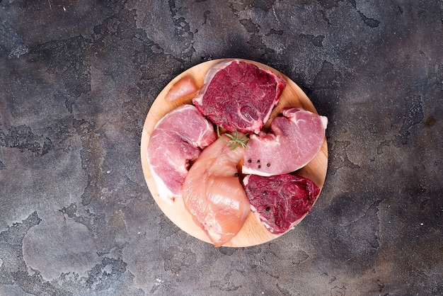 O modelo da galinha, da carne e da carne de porco crus na placa de corte ajustou-se na placa redonda de madeira. Proteínas magras.