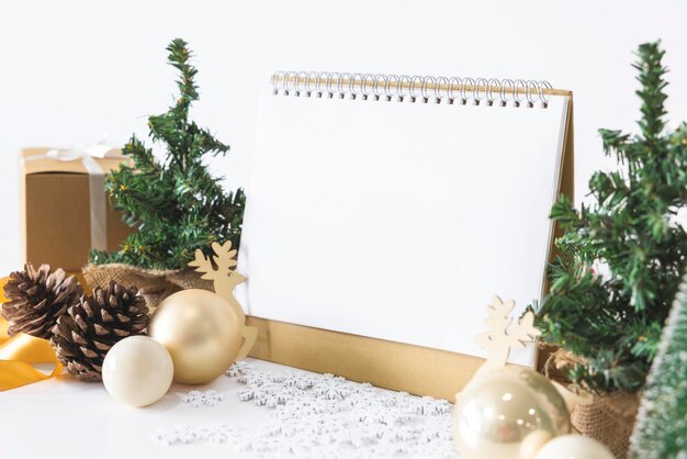 O modelo de calendário branco para inserir texto pela cena festiva da bela árvore de Natal adornada com bolas de Natal cones de pinheiro caixa de presente de casa vermelha amarrada fita dourada conceito sobre dia importante