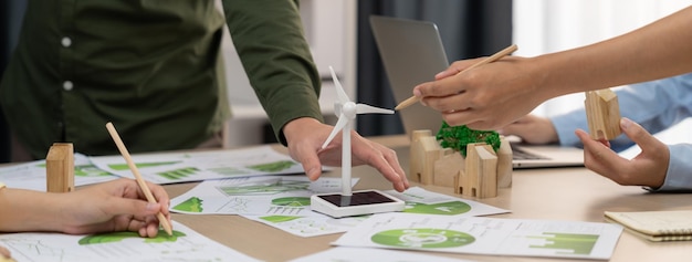 O modelo do moinho de vento representou energia renovável e o bloco de madeira representou a cidade ecológica foi colocado na mesa de reuniões de negócios verdes com documentos ambientais espalhados ao redor Delineamento da vista frontal