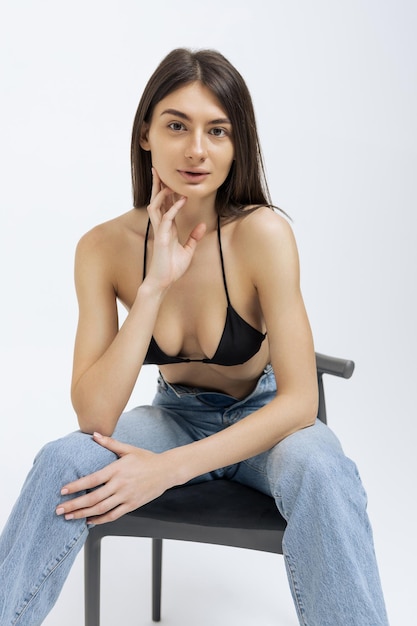 O modelo está sentado em uma cadeira em um top preto e jeans Fundo branco isolado Fotografia publicitária