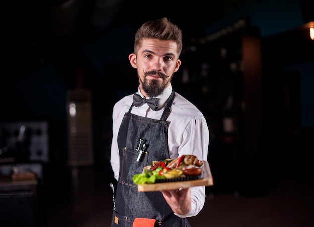 O mordomo de bigode segura o prato com o prato preparado em um evento festivo.