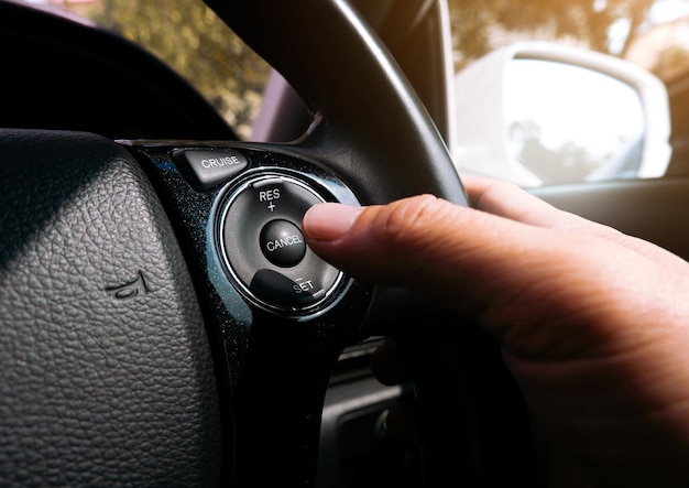 O motorista pressiona o botão de controle de cruzeiro no volante do carro com a mão