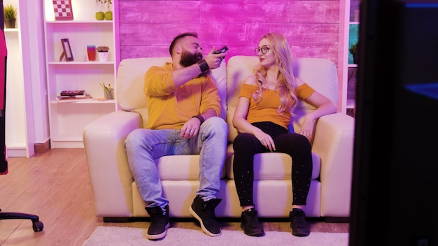 O namorado vence a namorada enquanto joga videogame usando controles sem fio, sentado no sofá.