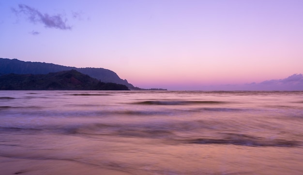 O nascer do sol ilumina o céu do amanhecer acima da Baía de Hanalei com a costa de Na Pali ao fundo perto de Hanalei Kauai Hawaii