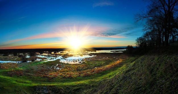 O nascer do sol panorâmico sobre a margem do rio com cores brilhantes vai muito bem para o cabeçalho do site