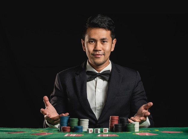 O negociante de homem asiático ou croupier embaralha as cartas de pôquer apostando no cassino no fundo preto da mesa verde convite do negociante homem aposta jogando cartas conceito de jogo de pôquer de pôquer de cassino