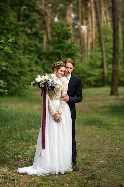 O noivo abraça a noiva por trás na floresta