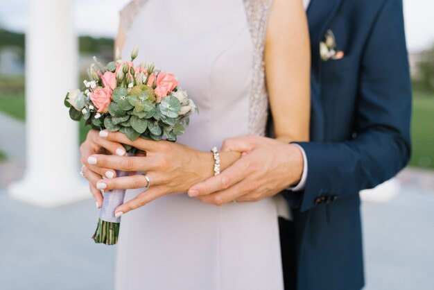 O noivo abraça a noiva, uma visão ampla das mãos. a noiva tem um delicado buquê de flores nas mãos