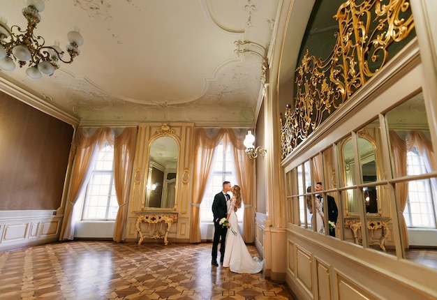 O noivo beija a noiva e ela segura um buquê de casamento. sala com um belo interior com muitos espelhos e grandes janelas.