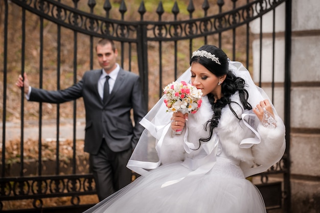 O noivo e a noiva no parque do outono estão perto de portão de ferro