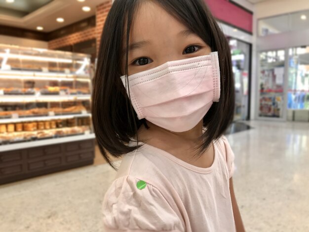 O novo Coronavirus / Covid-19 normal é um teste de temperatura e triagem. Menina asiática feliz com máscara cirúrgica tem um adesivo verde para passar em verificações de temperatura corporal no supermercado