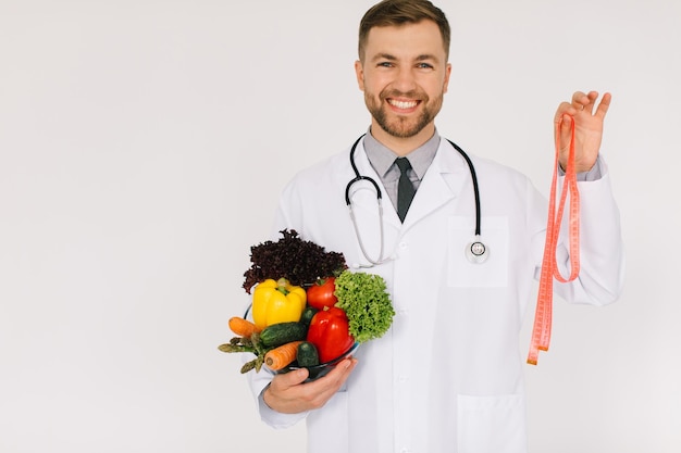 Foto o nutricionista médico masculino com estetoscópio segurando legumes frescos e régua em fundo branco