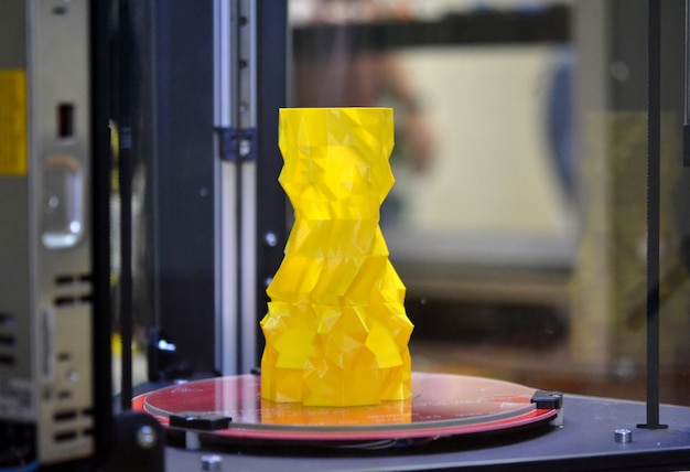 O objeto na forma de um vaso amarelo fica na impressora 3d de mesa