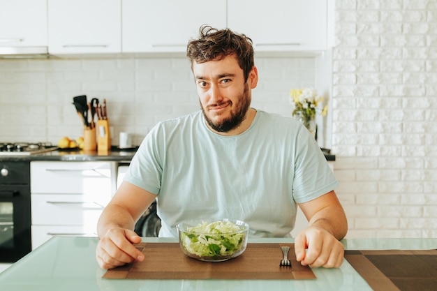 O olhar astuto de um jovem que está sentado na cozinha com uma tigela de salada piscando para mim veio