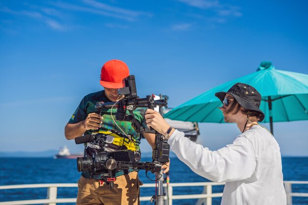 O operador da steadicam e seu assistente preparam a câmera e o estabilizador de 3 eixos para uma filmagem comercial