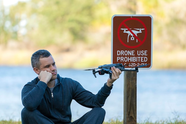 O operador está desapontado porque não pode pilotar seu quadricóptero no parque nacional sem área de drones O homem não consegue usar seu UAV perto do sinal de aviso de restrição