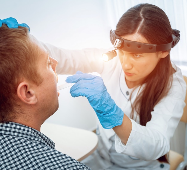 O otorrinolaringologista examina a garganta do homem com uma espátula.