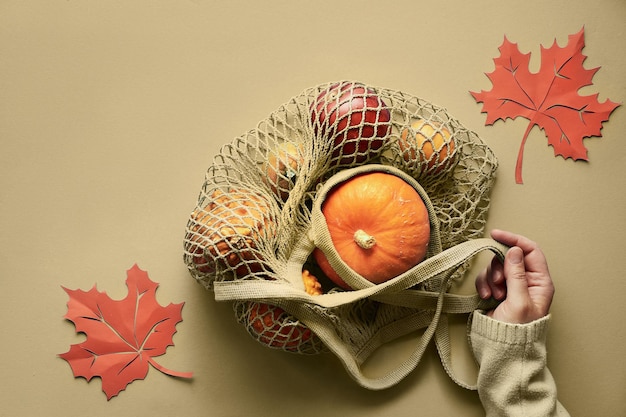O outono plano deitar-se com as mãos femininas de suéter azul e bolsa de barbante turquesa com abóboras laranja. Vista superior em plano de fundo de papel na cor azul menta.