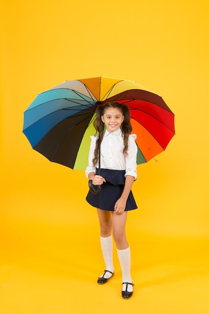 O outono vem com as mudanças climáticas Criança pequena segurando guarda-chuva colorido para chuva de outono em fundo amarelo Criança indo para a escola no dia de outono ou 1º de setembro Preparando-se para o outono