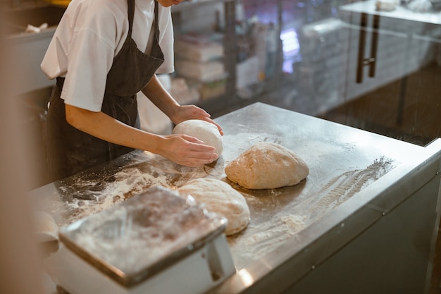 O padeiro amassa a massa para o pão na mesa em closeup de confeitaria artesanal