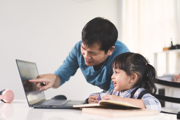 O pai asiático está ajudando e apoiando a filha a estudar a lição da aula on-line.