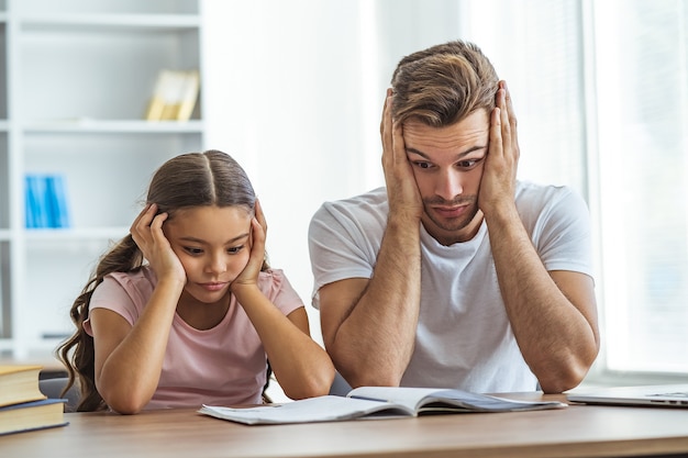 O pai cansado e uma filha fazendo lição de casa na mesa