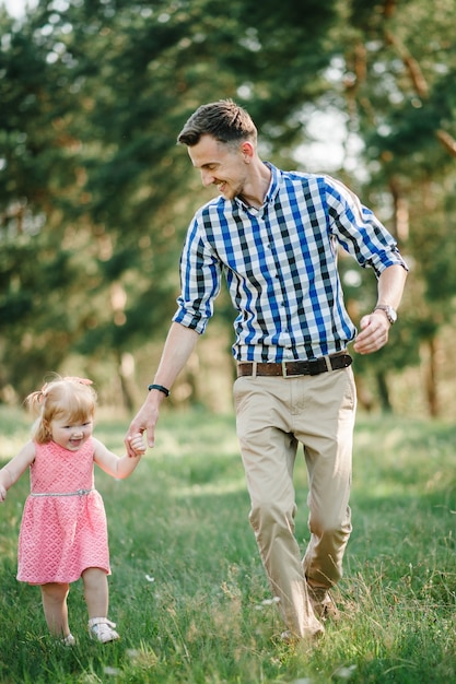 O pai corre com uma filha e segura a natureza dela nas férias de verão. Pai e filha andando e brincando no parque na hora do sol. Conceito de família amigável. Fechar-se.