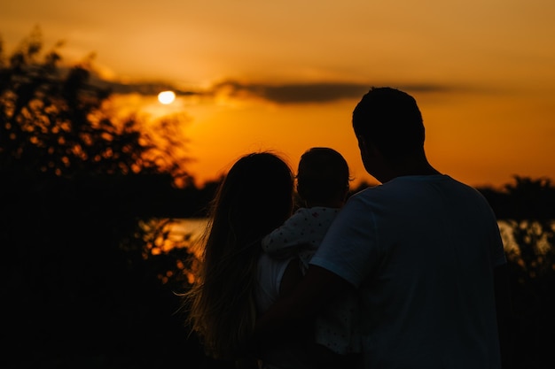 O pai da mãe mantém a filha afastada e olhando o pôr do sol Retrato de uma jovem família na natureza de férias ao ar livre O conceito de férias em família