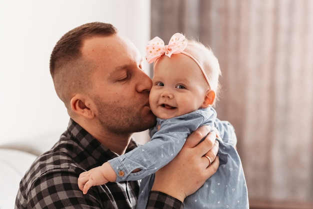 O pai de um jovem bonito beija uma filha. Menina nos braços do papai