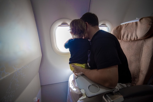 O pai e a linda criança sentam-se em um avião e olham para o céu pela vigia no primeiro voo